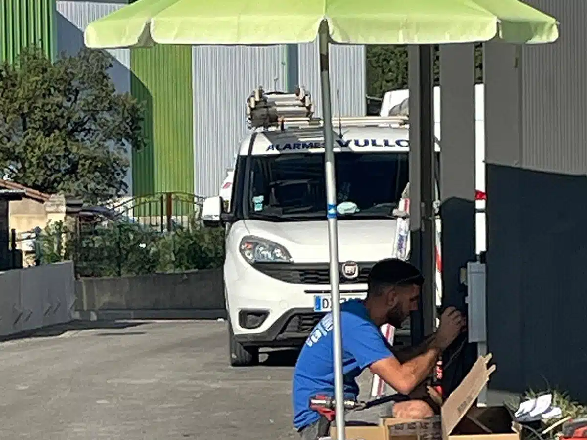 Homme de l’équipe Vullo travaillant à l’ombre sous un parasol sur une boîte de contrôle.