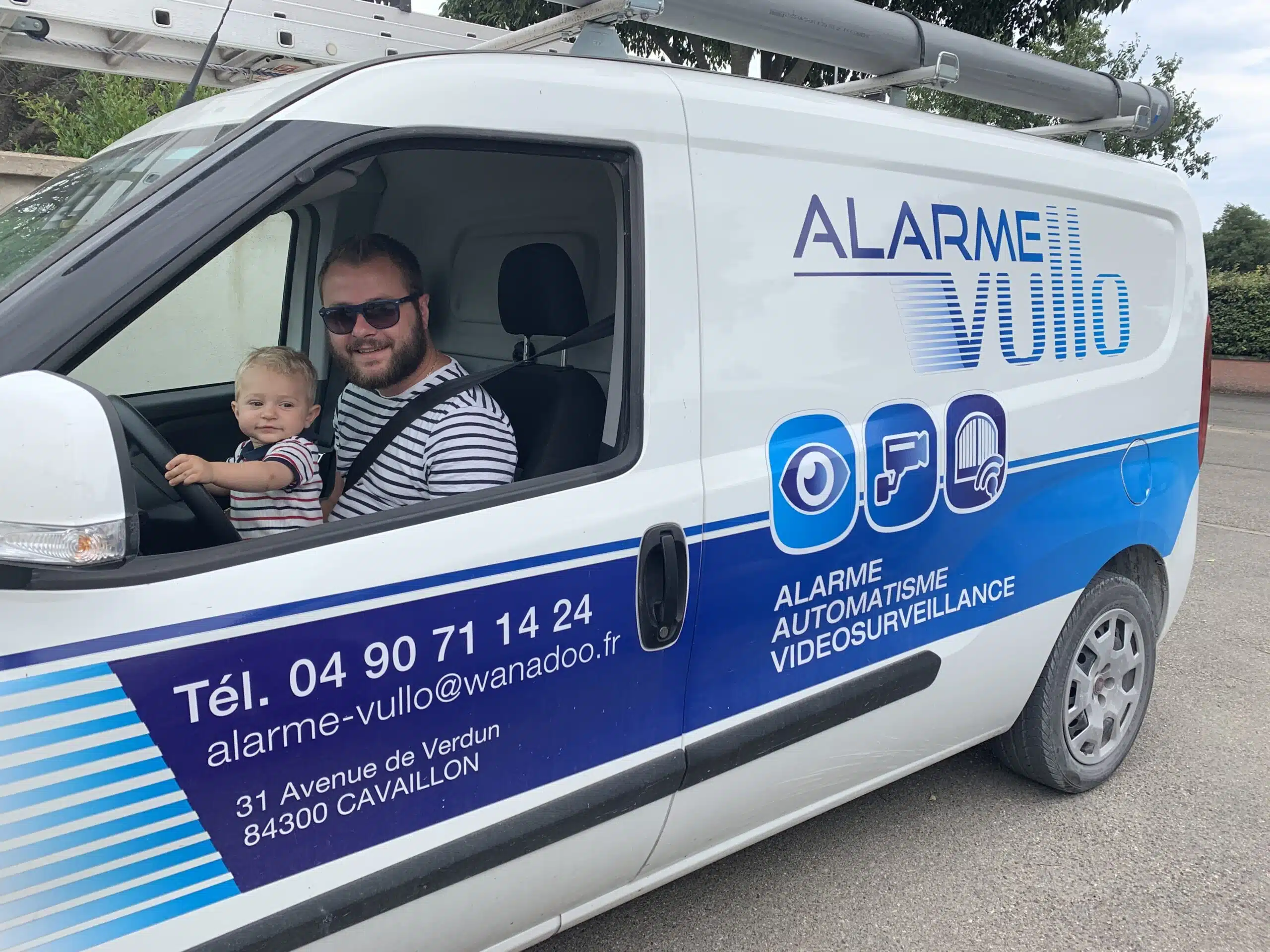 Petit garçon sur les genoux de son père dans une voiture de fonction avec alarme Vullo.