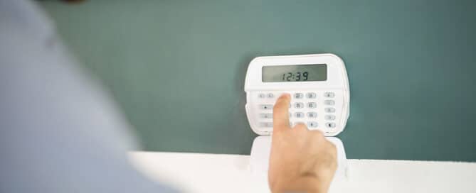 Gros plan sur la main d'un homme qui tape un code sur un clavier pour armer son système d'alarme domestique.