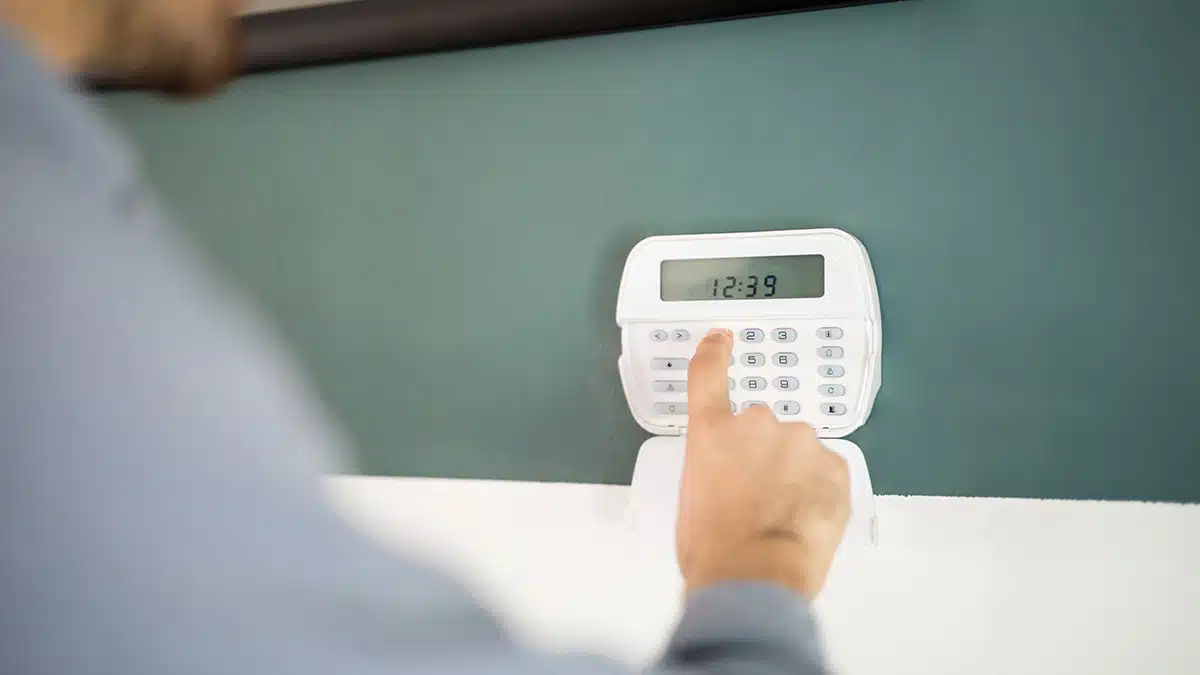 Gros plan sur la main d'un homme qui tape un code sur un clavier pour armer son système d'alarme domestique.