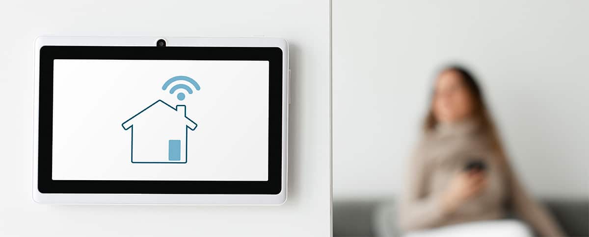 Un panneau de contrôle de gestion d'alarme centralisé est affiché sur un mur au-dessus d'un smartphone qui affiche une application de maison connectée.