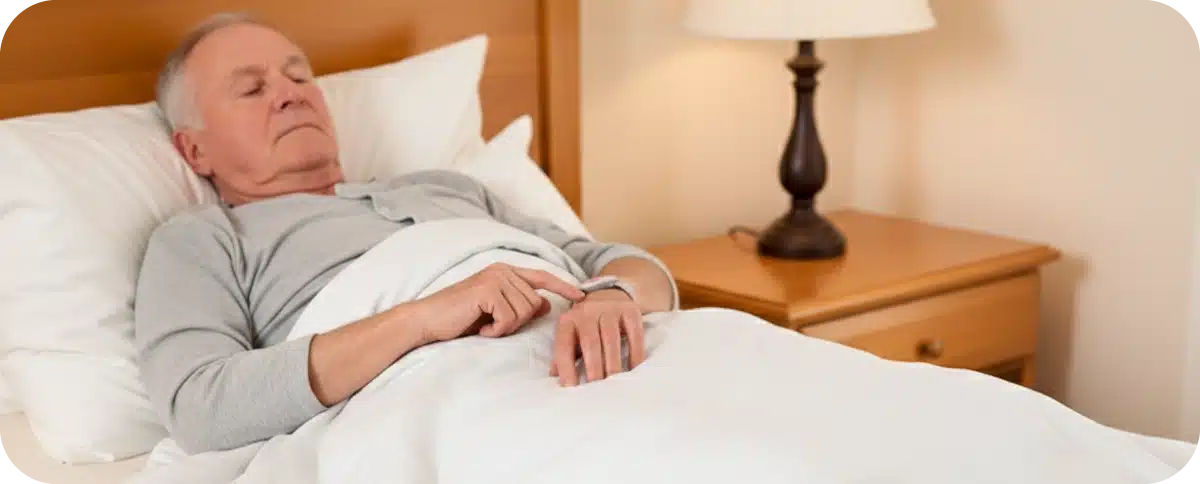 bouton-alarme-medicale Homme senior dormant dans son lit avec un bracelet d'alarme médicale au poignet.